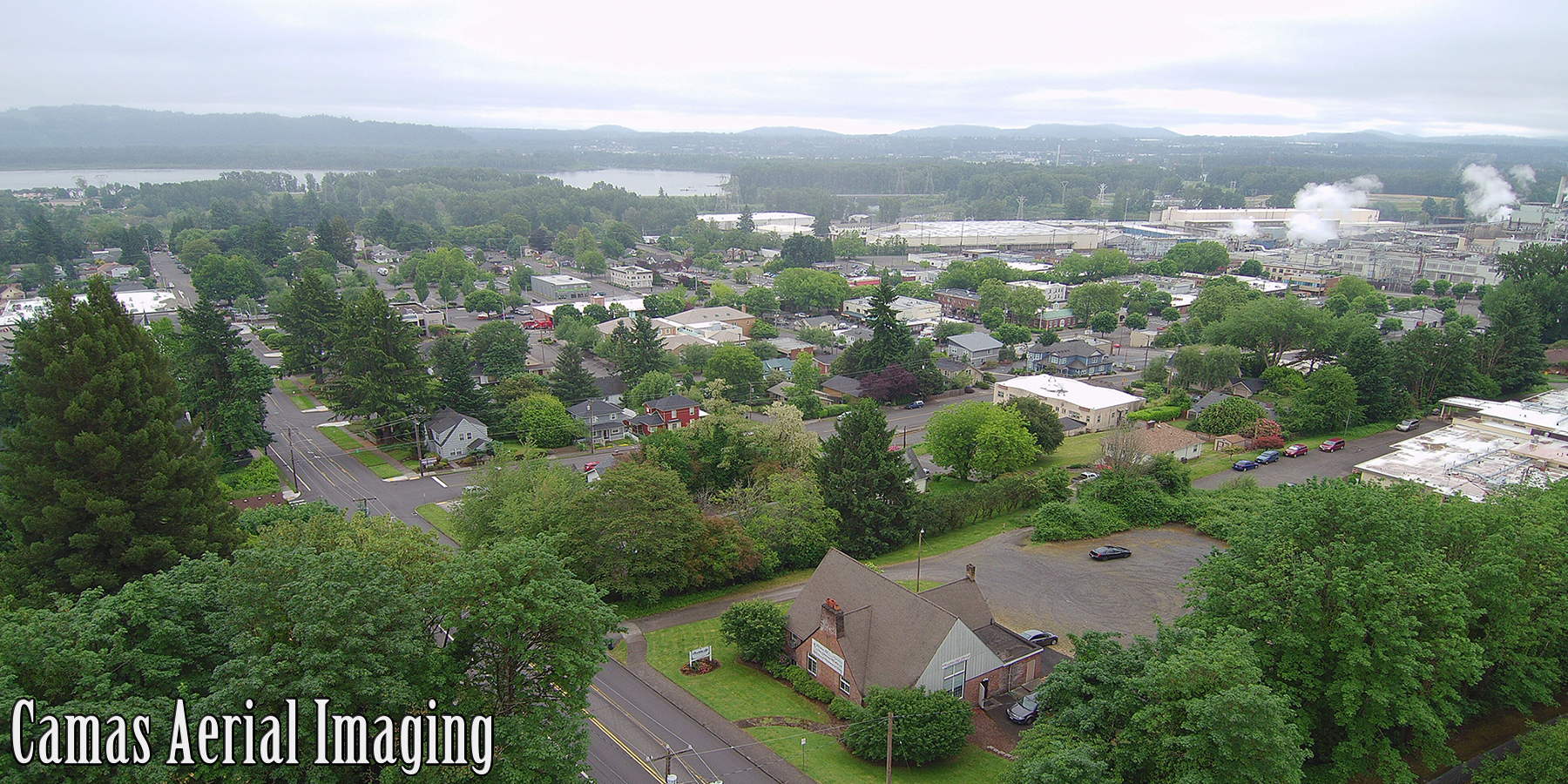 Downtown Camas looking South-Southwest from the intersection of 14th and Garfield, one can make out the abundance of trees in this long developed area, along with the well known Camas Paper Mill, the Columbia River, and the hills south of the Portland Metropolitan Area.